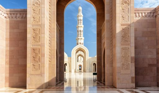 Amazing view of minaret through scenic arches of the Sultan Qaboos Grand Mosque in Muscat, Oman. Beautiful Islamic architecture. The Muslim place is a popular tourist attraction of the Middle East.